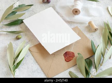 Wedding invitation cards and envelopes on a white marble table with olive branches close up. Elegant modern template with horizontal blank paper cards Stock Photo