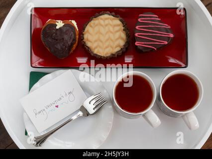 Valentine's tea with tea cups and gourmet mini cakes on a platter and note card on dish with forks; Studio Shot Stock Photo