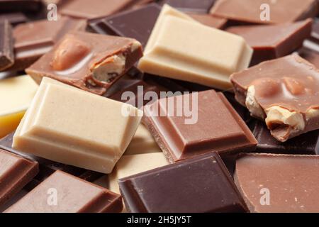 Pile of brocken pieces dark milky and white chocolate with nuts. Stock Photo