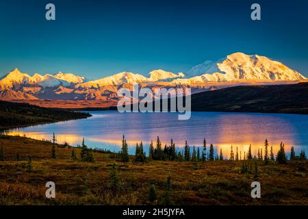 Sunset glow on Mount Denali (McKinley) reflects on Wonder Lake with blue sky, Denali National Park and Preserve in autumn, Interior Alaska Stock Photo