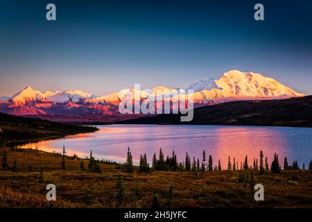 Sunset glow on Mount Denali (McKinley) reflects on Wonder Lake with blue sky, Denali National Park and Preserve in autumn, Interior Alaska Stock Photo