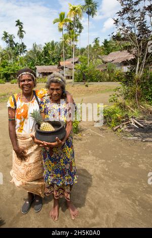 Two women with pineapple in Mou Village, Morobe Bay, Morobe Province, Papua New Guinea; Mou, Morobe Province, Papua New Guinea Stock Photo