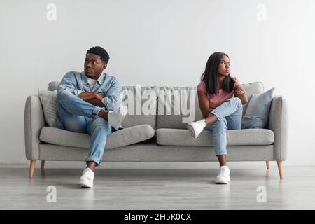 Family Conflict Concept. Stubborn black couple sit on couch back to back avoid talking after fight, offended man and woman separated on sofa ignoring Stock Photo