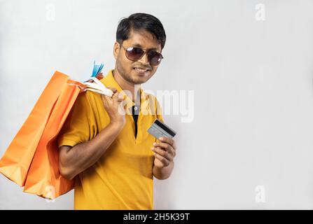 A middle aged Indian man in yellow dress with shopping bags and credit card smiling at the camera on white background Stock Photo