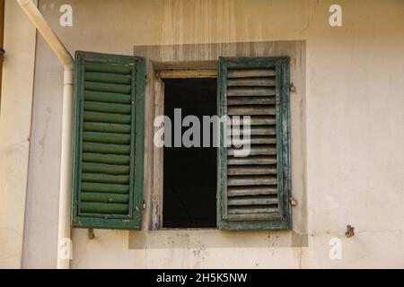 Green shutters on the window against a yellow colored wall. Old exterior in italian mediterranean village with closed Wooden vintage window with green Stock Photo