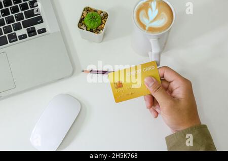 Top view man holding a credit card and on the desk. Laptop computer Notepad and pen.Online shopping business, pay by credit card. Stock Photo