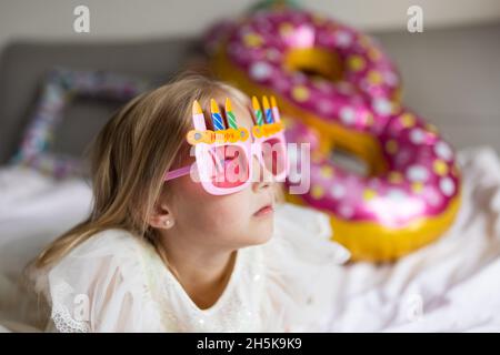 Indoor shot of pretty joyful cute adorable girl kid celebrating eight years old birthday with bright and colorful balloons with inscription words stay Stock Photo