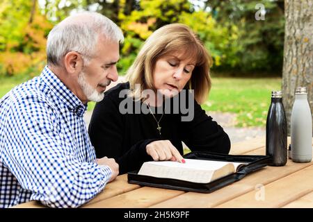 A mature couple sharing devotional time together and studying the bible at a picnic table on a warm fall day in a city park Stock Photo