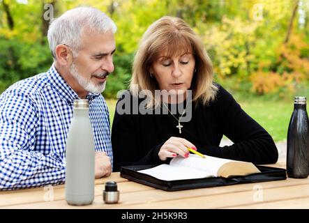 A mature couple sharing devotional time together and studying the bible at a picnic table on a warm fall day in a city park Stock Photo