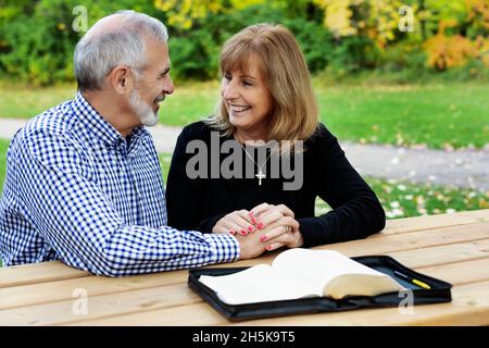 A mature couple sharing devotional time together and studying the bible at a picnic table on a warm fall day in a city park Stock Photo