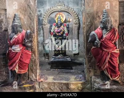 Alcove with Hindu deity statue in wall with guardian statues wrapped in silk on either side at the Dravidian Chola era Airavatesvara Temple Stock Photo