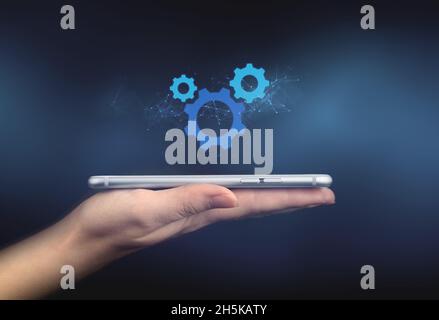 Mobile phone and settings icon. Digital marketing concept. Modern wireless technology and communication. Hand with smartphone on a black background ph Stock Photo