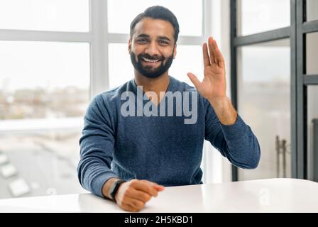 Video meeting with a happy indian man, cheerful guy waving and looking at the camera on a screen. Middle-aged multiracial eastern male employee takes a part in virtual conference, video call Stock Photo