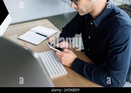 Cropped view of programmer using smartphone near computers and notebook in office Stock Photo