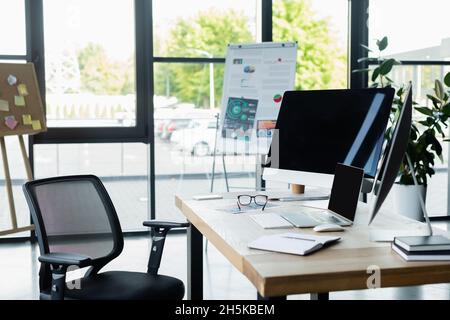 Computers with blank screen near notebook and eyeglasses on table in office Stock Photo