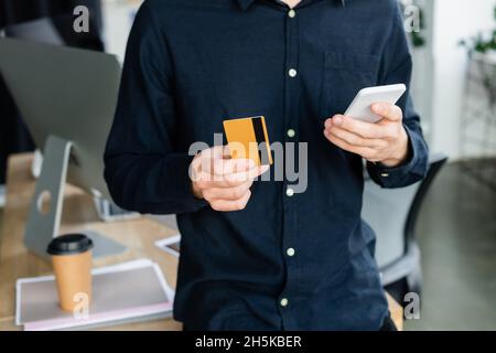 Cropped view of programmer using smartphone and credit card in office Stock Photo