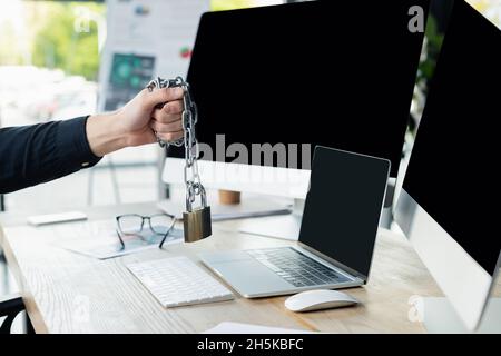 Cropped view of programmer holding padlock on chain near computers with blank screen in office Stock Photo