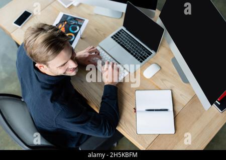 Overhead view of smiling developer using computers near smartphone and notebook on table Stock Photo