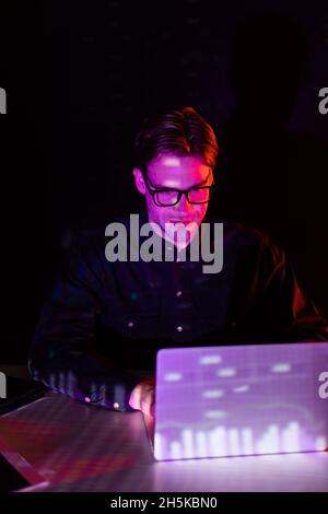 Programmer in eyeglasses looking at laptop with charts reflection isolated on black Stock Photo