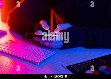 Cropped view of programmer using smartphone near computer keyboard and document on black background Stock Photo