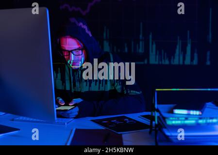 Hacker with charts reflection using smartphone near computer and documents on black background Stock Photo