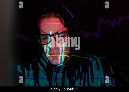 Displeased hacker with charts reflection looking down on black background Stock Photo