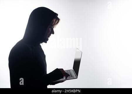 Side view of hacker in hood using laptop with blank screen isolated on grey Stock Photo