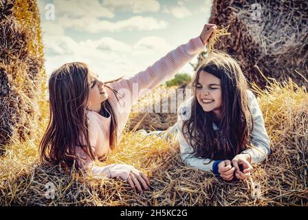 Two young sisters spending quality time together while lying on hay bales on their family farm; Alcomdale, Alberta, Canada Stock Photo