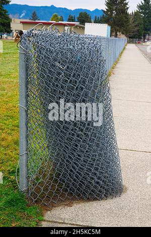 Rolled chain link fencing along a sidewalk beside an Elementary school in Maple Ridge, B. C., Canada. November 2021. Stock Photo