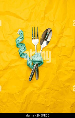 Steel spoon a fork and measuring tape on yellow paper texture background Stock Photo