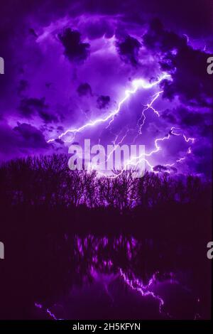 Lightning bolts illuminating a moody night sky reflecting in the water; Nebraska, United States of America Stock Photo