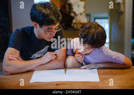 A boy and father sit together at kitchen table doing homework Stock Photo