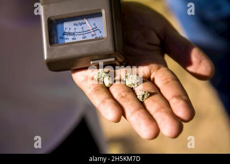 Geiger counter and trinitite in a human hand. Stock Photo