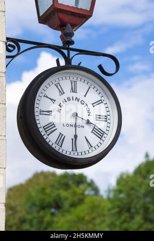 Close up of vintage Kensington railway clock on platform of UK heritage railway station in summer with blue sky & fluffy clouds background. Stock Photo