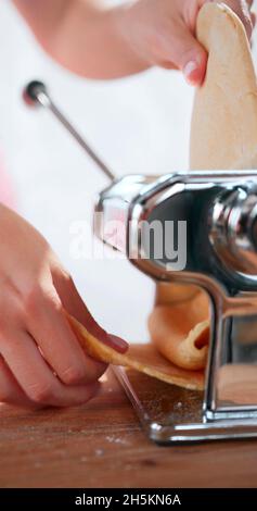 A vertical photo of a woman who is using a pasta maker Stock Photo