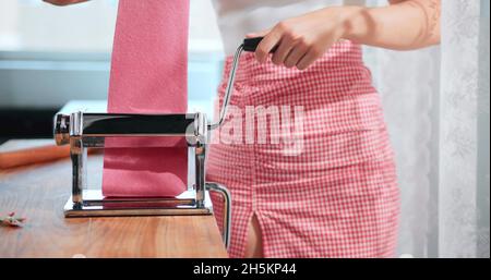 A woman is using a pasta maker with a pink pasta Stock Photo