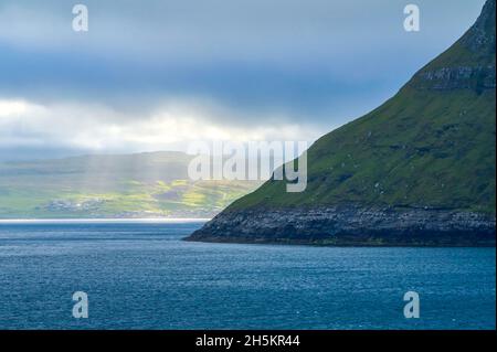 View from the island ferry Norrona when driving through the Faroe Islands, with sunlight streaming through the clouds to the water and land below Stock Photo