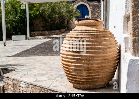 Handmade old ceramic amphora with cover in a garden, traditional clay craft container. Greek island house exterior decoration, Chora village Greece. Stock Photo