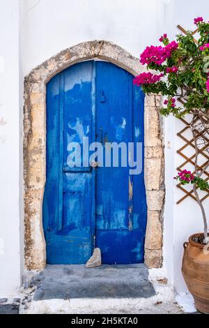 Greek island typical architecture. Kythira Chora town, Greece. Blue wooden door and red bougainvillea on whitewashed house wall. Sunny summer day Stock Photo