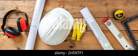 Architect engineer office desk, construction building drawings and safety equipment on a wooden table. Top view, banner Stock Photo