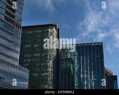 Low angle view of modern high-rise office buildings with glass facades and waving Canadian national flags in district Coal Harbour in Vancouver. Stock Photo