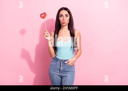 Portrait of attractive comic girl holding sweet heart candy sending air kiss isolated over pink pastel color background Stock Photo