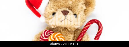 Bunner with stuffed toy Teddy bear in a red Santa Claus hat on one ear, holding candy cane and two striped lollipops in its paws. White background, co Stock Photo