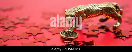 Banner with a bronze figure of a tiger with coin - symbol of the Chinese new year 2022 on a red background with stars, copy space. Stock Photo