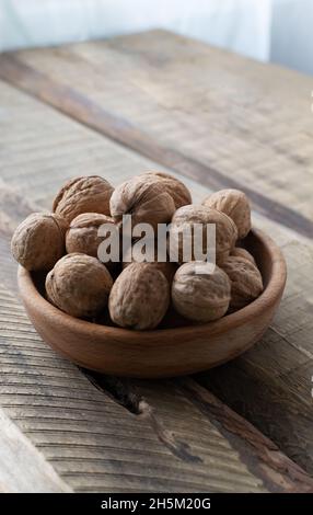 Dry Walnuts lie in a wooden bowl on a wooden table. Rustic style. Healthy nutrition concept. Vertical orientation. Copy space. Stock Photo