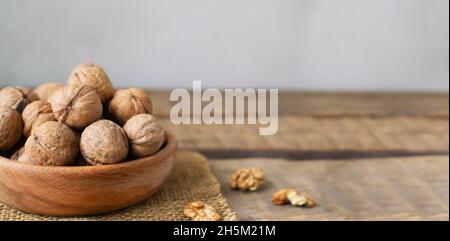 Dry Walnuts lie in a wooden bowl and several nuts are chopped on a wooden table. Rustic style. Vegetarian food concept. Horisontal orientation. Banner Stock Photo