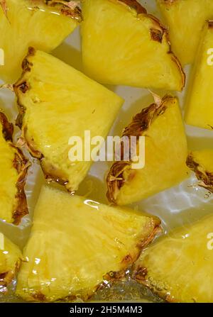Pineapple close-up in liquid with bubbles. Slices of ripe pineapple in water. Close-up fresh slices of yellow pineapple on white background. Vertical Stock Photo