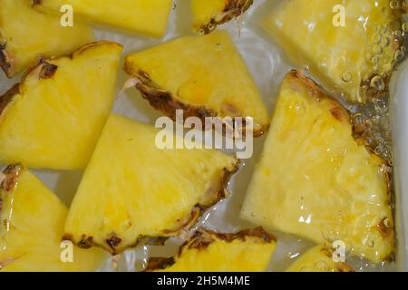 Slices of pineapple in water on white background. Pineapple close-up in liquid with bubbles. Slices of ripe pineapple in water. Macro image of fruits Stock Photo