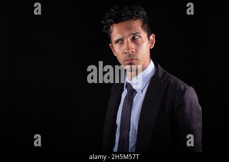Businessman suspicious of something he looks askance at. Young latin with suspicious look and expression, looking for something. Isolated on a black Stock Photo