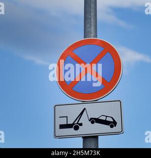 Close-up shot of No Parking and Evacuation on tow truck road signs on a pole against a blue sky Stock Photo
